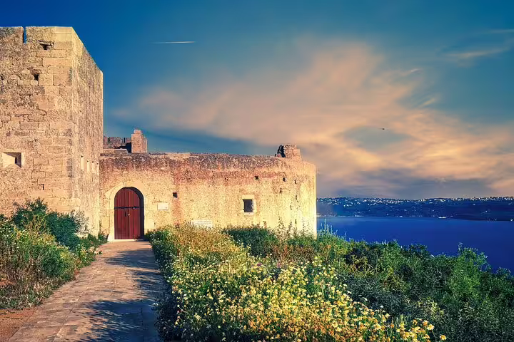 Historic stone fortress overlooking the sea at sunset, surrounded by wildflowers, part of a Crete countryside private tour.