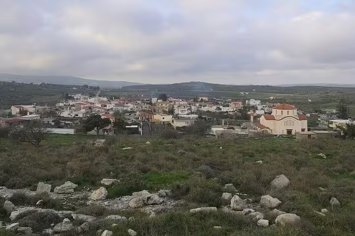 Scenic view of a traditional village near Heraklion, Crete, surrounded by lush vineyards under a cloudy sky, perfect for wine tours.