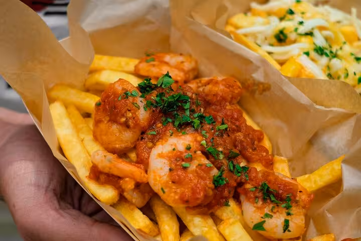 Crispy fries topped with shrimp in a rich tomato sauce, a savory treat from Medellín's vibrant street food scene.