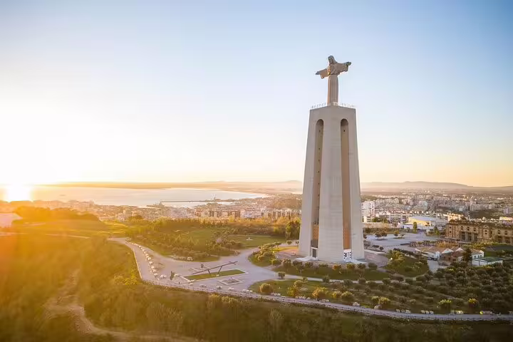 A breathtaking view of the Cristo Rei statue overlooking Lisbon at sunrise, highlighting the scenic beauty of the Arrábida & Sesimbra tour.