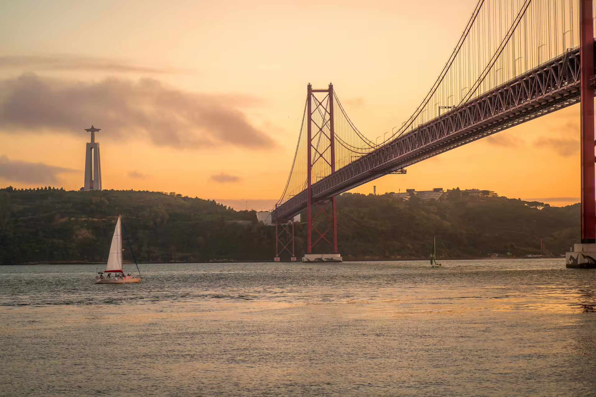 Sunset view of the 25 de Abril Bridge and Cristo Rei statue over Tagus River, perfect for Arrábida & Sesimbra day trips.
