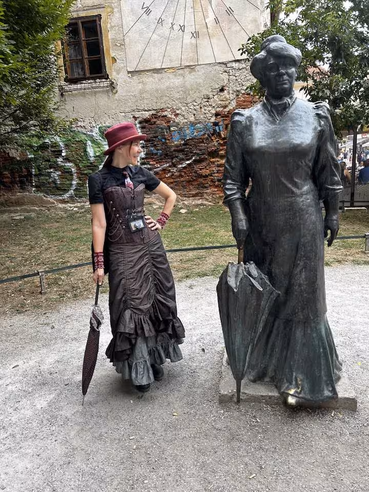 Woman in Victorian steampunk costume with umbrella posing beside bronze statue in Croatia