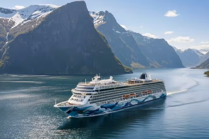 Large cruise ship sailing through a scenic Norwegian fjord with snow-capped mountains in the background