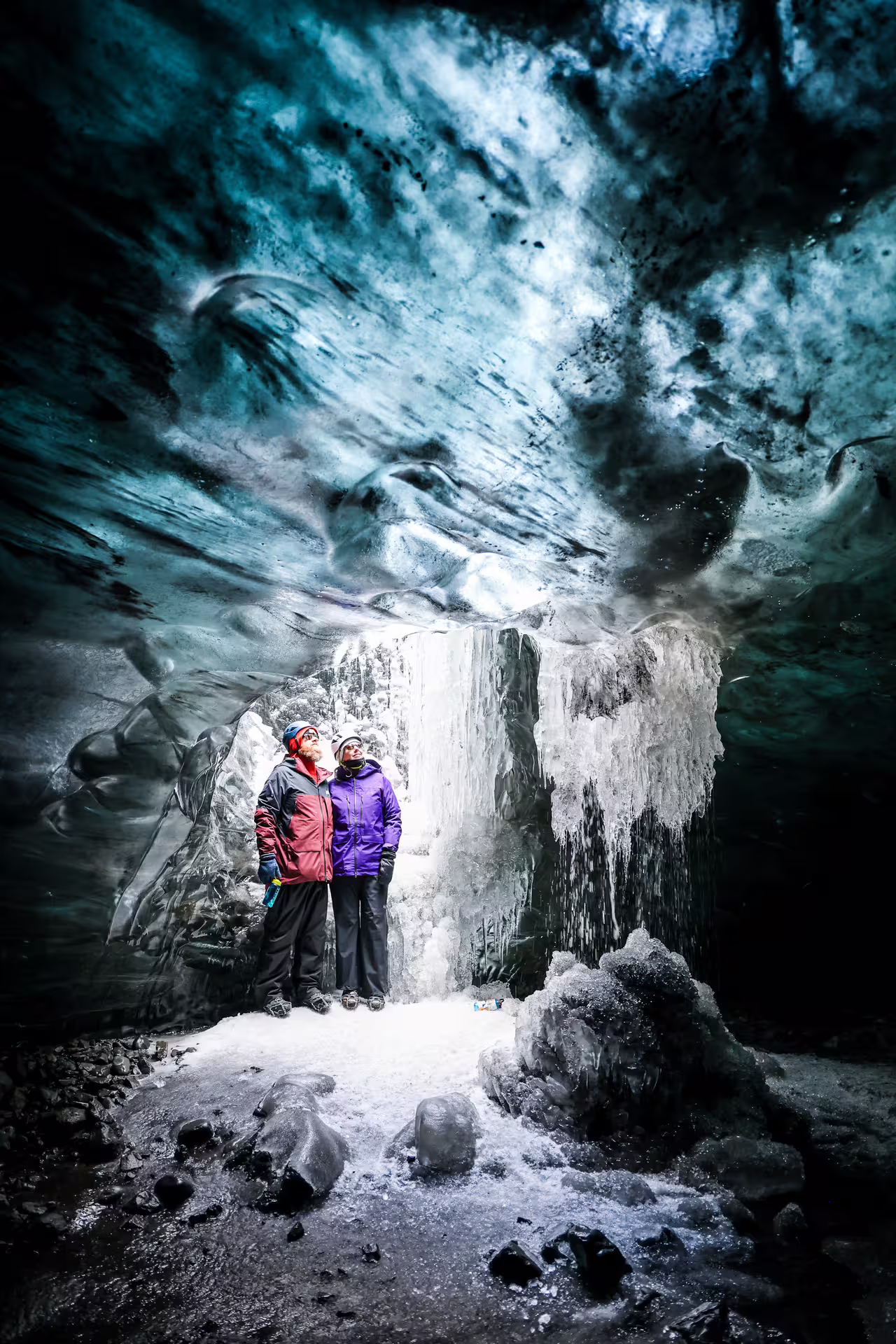 Two guests in helmets marveling at a frozen ice waterfall during a guided crystal ice cave tour in Iceland