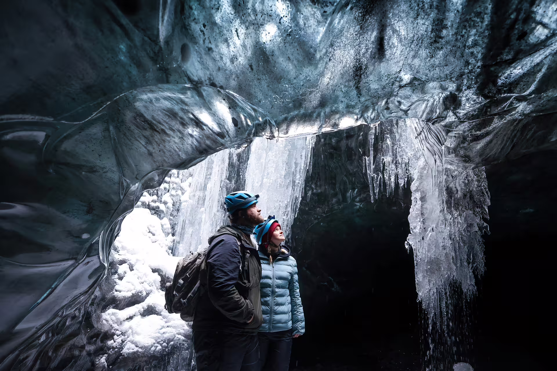 Two helmeted explorers marvel at stunning blue ice formations inside a crystal ice cave on Vatnajokull Glacier Iceland.