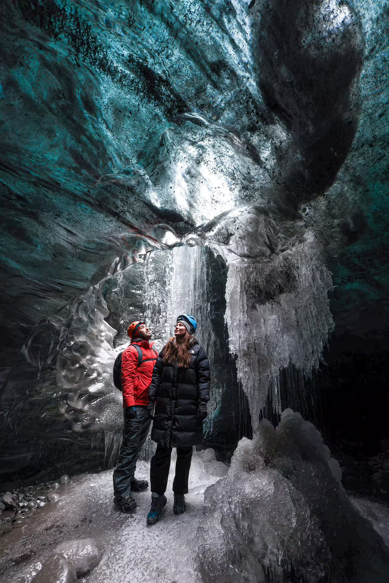 Couple in helmets marvels at towering ice formations inside a crystal ice cave on Vatnajokull Glacier Iceland
