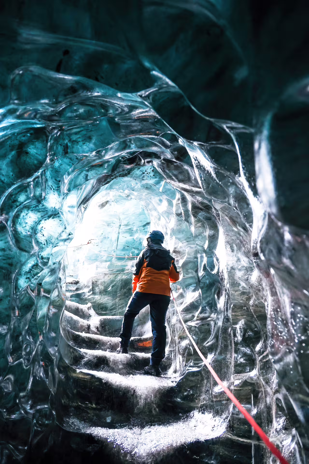 Explorer in orange jacket standing inside glowing crystal ice cave tunnel on Vatnajokull Glacier guided tour