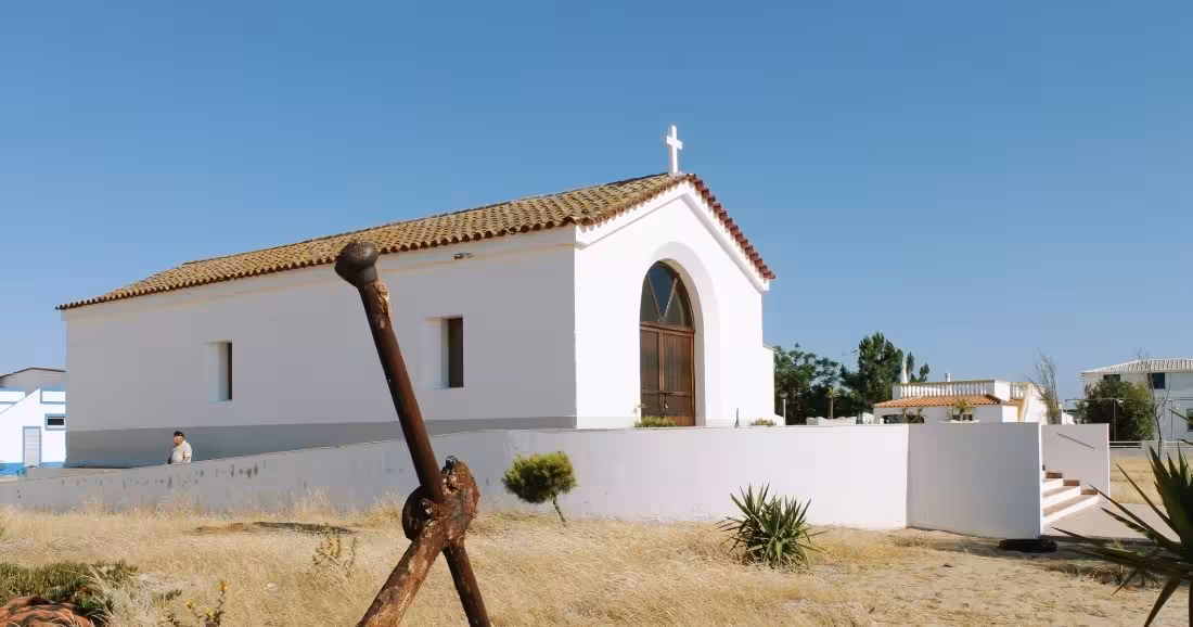 A whitewashed chapel with a cross and rustic anchor on Ilha da Culatra during a Ria Formosa boat tour stop