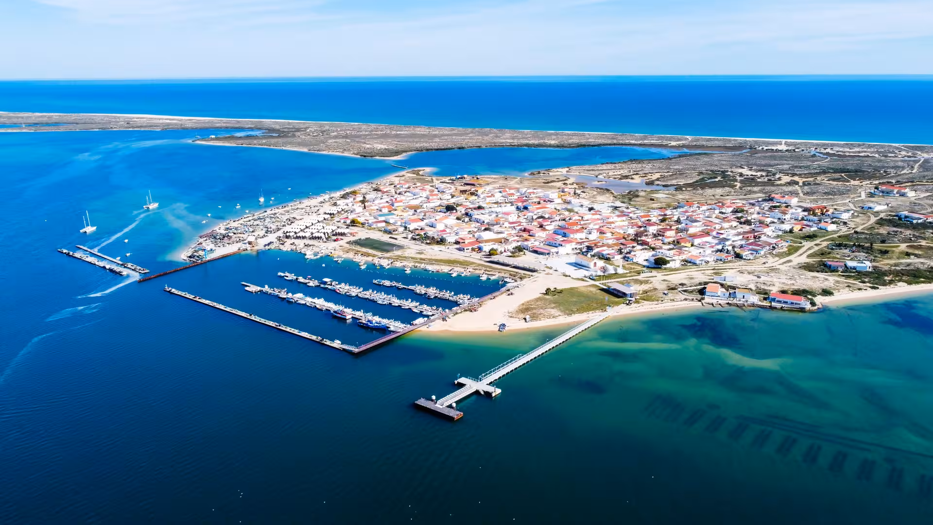 Aerial view of Culatra Island marina and pier surrounded by turquoise waters in Ria Formosa Natural Park Algarve