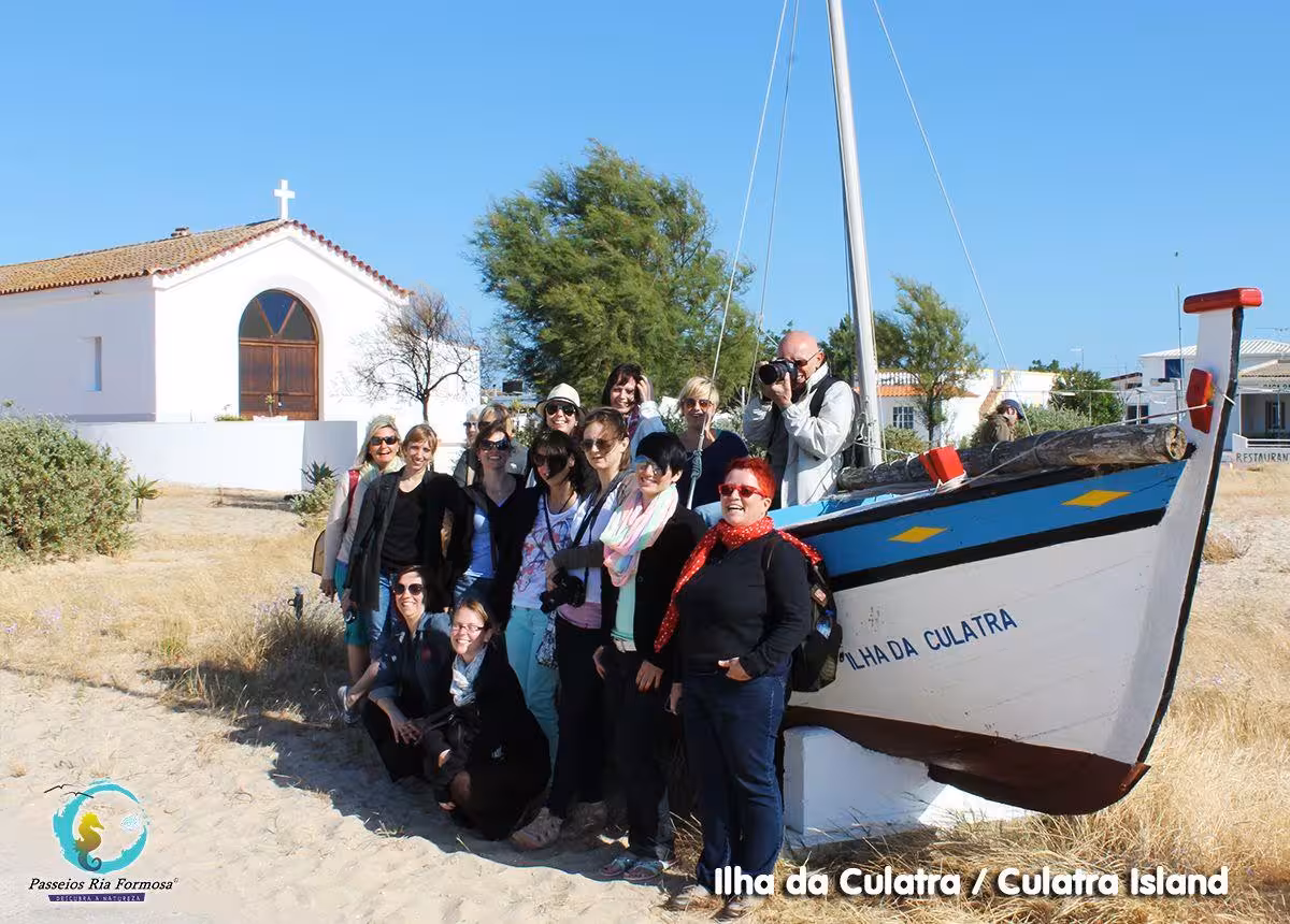 Tour group posing by traditional boat at Culatra Island chapel on scenic Ria Formosa boat tour Olhao