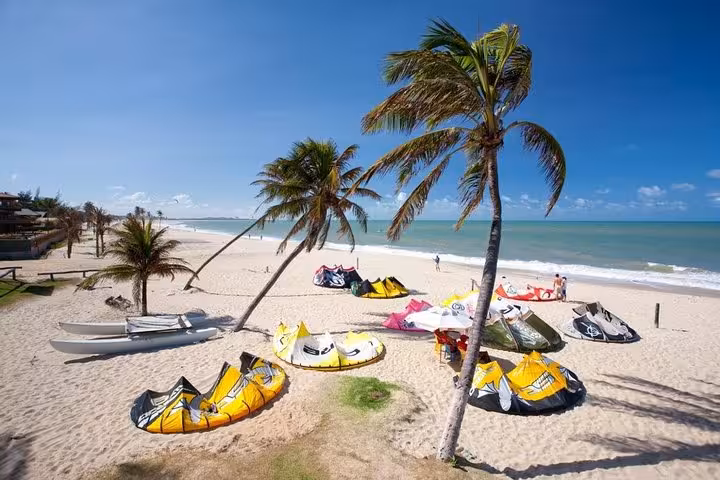 Cumbuco Beach Tour scene with colorful kitesurfing kites on white sand, palm trees and turquoise sea