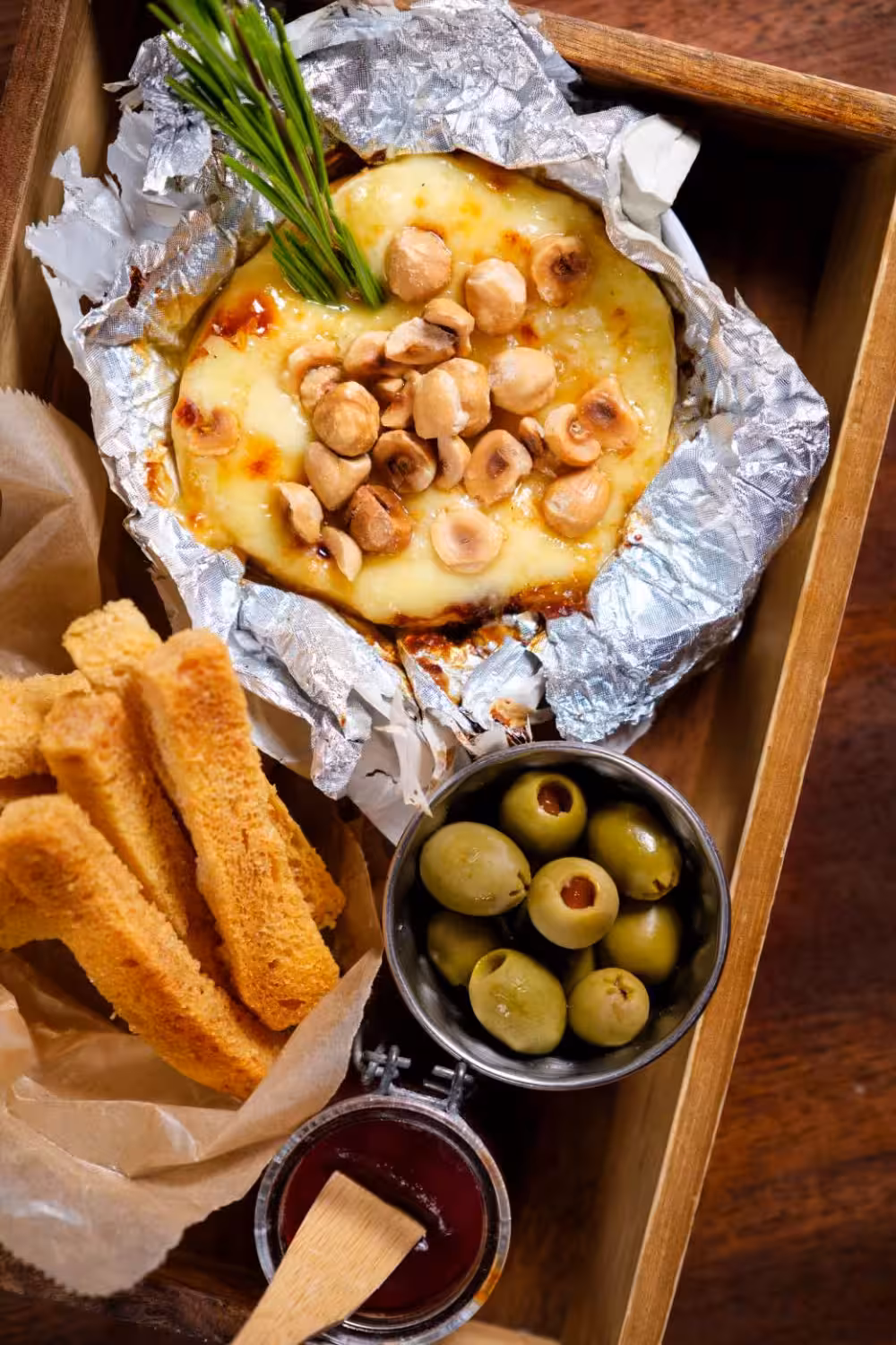 Rustic wooden tray with baked camembert topped with hazelnuts, olives, jam, and toasted bread for city tasting