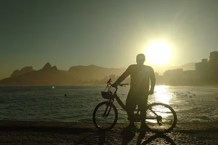 Cyclist silhouetted against sunrise at Ipanema Beach, Rio, during scenic bike tour along the vibrant coastline.