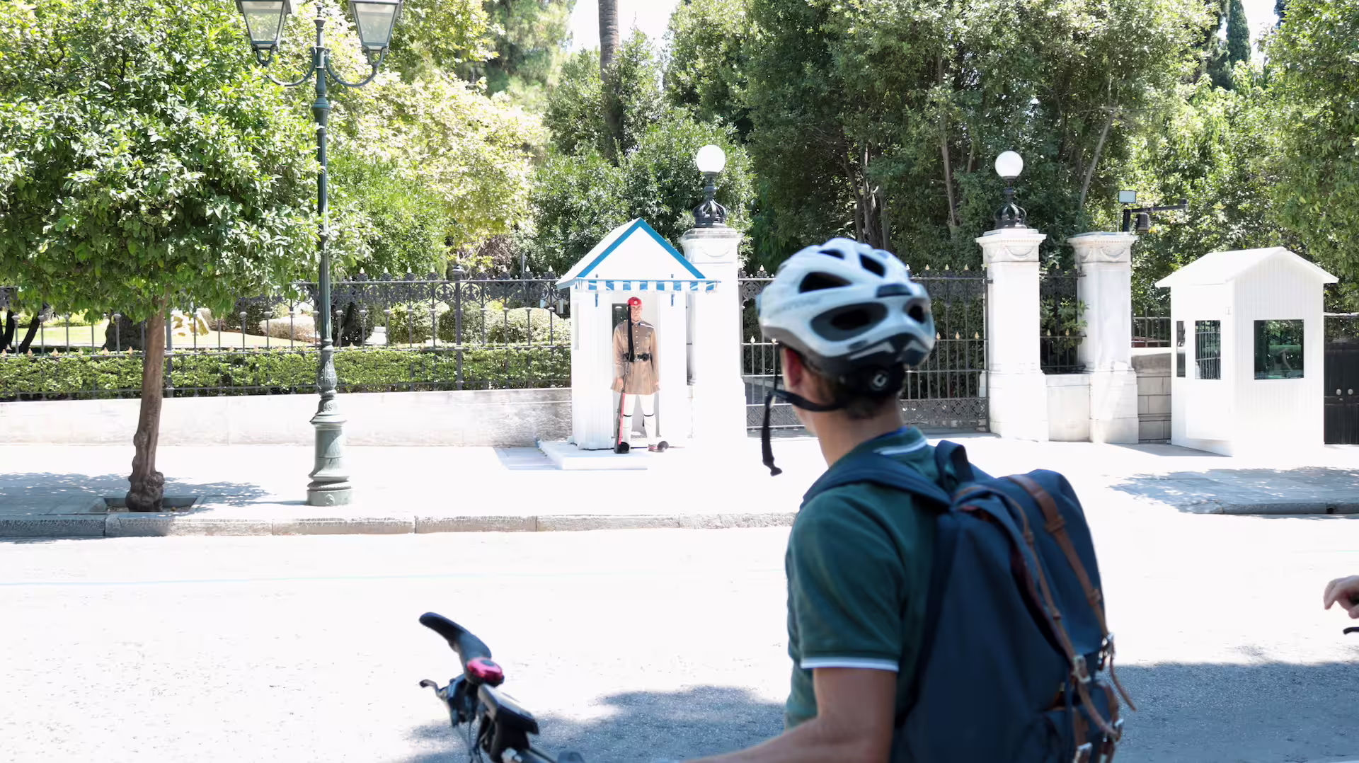 Cyclist observing traditional guard at a historic site in Athens under sunny skies.