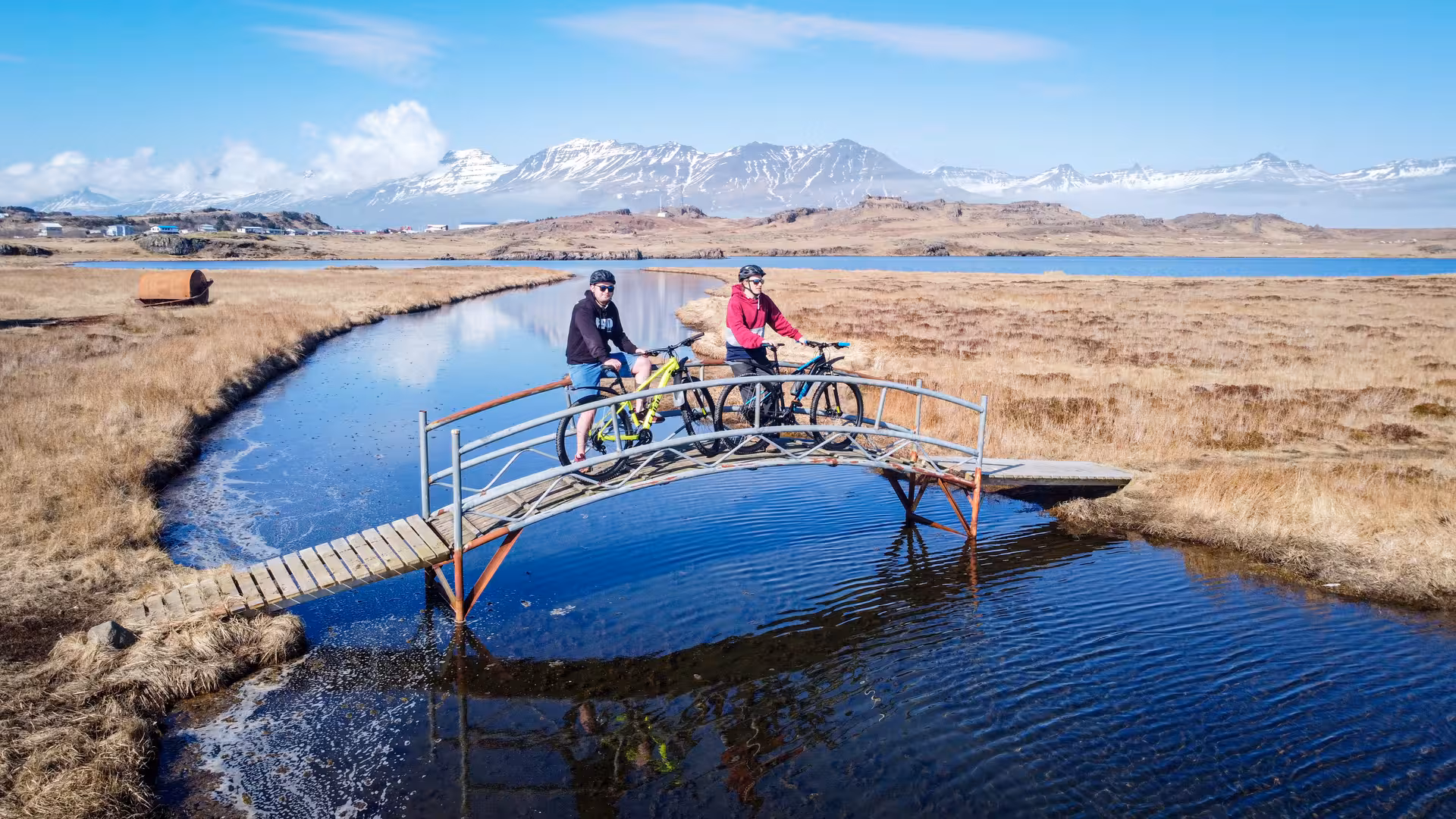 Two cyclists pause on a bridge amidst Iceland's breathtaking East Fjords landscape.