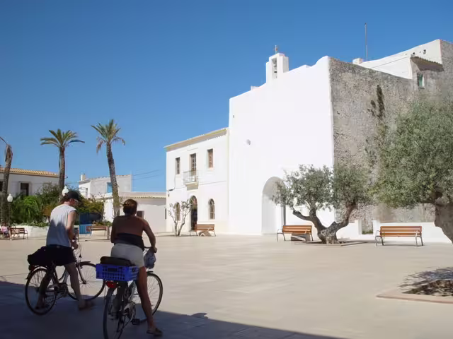 Cyclists in a Formentera village square with whitewashed buildings on Ibiza to Formentera bike day trip