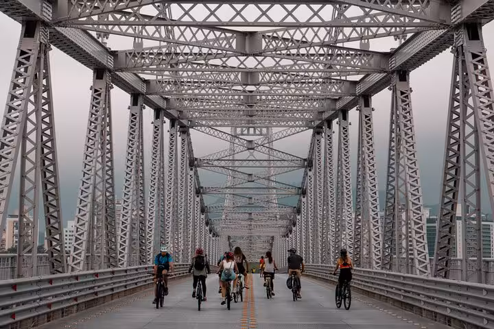 Cyclists crossing a metal bridge in Florianopolis, capturing scenic views on a photography and history bike tour.