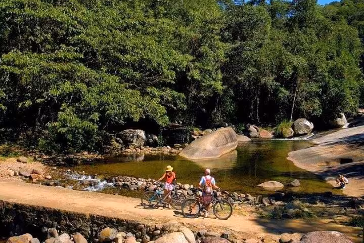 Two cyclists pause by a serene river surrounded by lush forest in Paraty, ideal for nature bike tours.