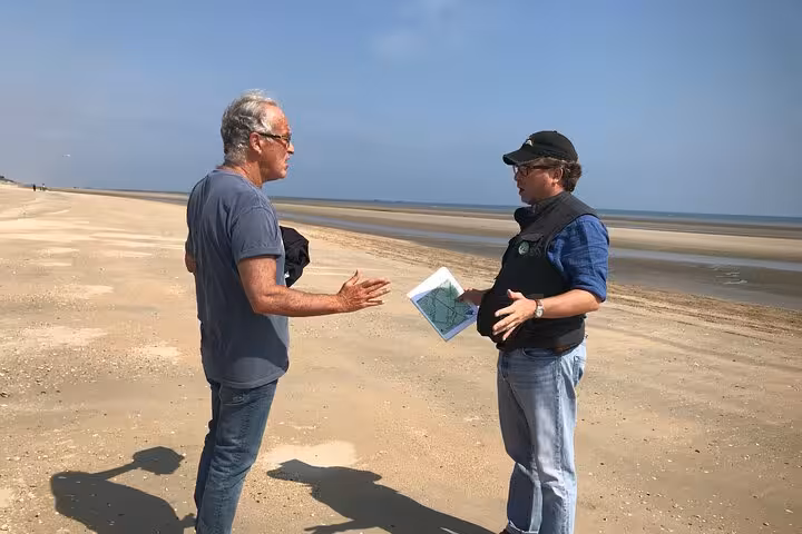 Two men discussing a map on the vast sandy D-Day beaches of Normandy on a clear day.