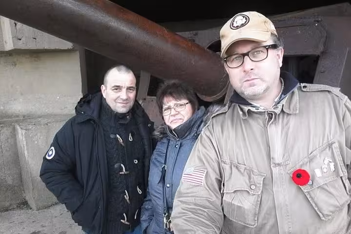 Three tourists posing beside a WWII cannon at Normandy D-Day beach fortification