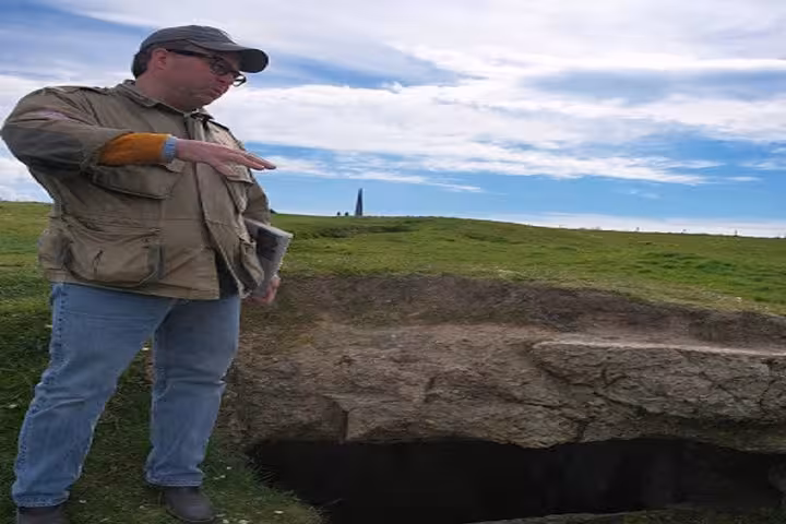 Tour guide pointing at WWII bunker excavation on D-Day beaches in Normandy