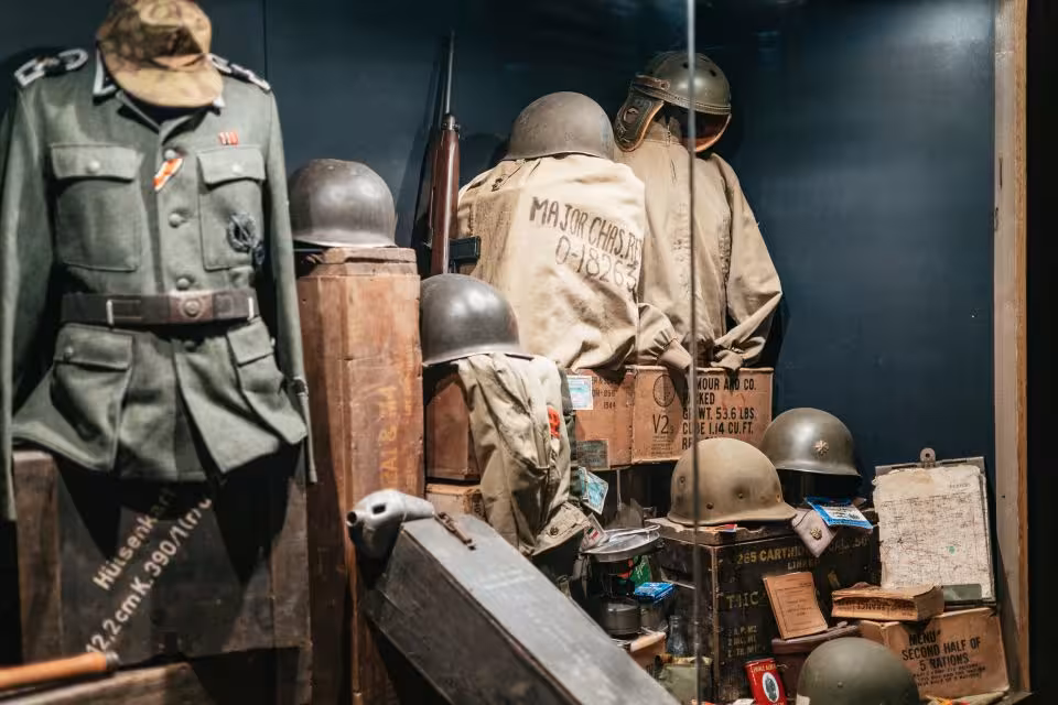 WWII museum display with Allied and German uniforms, helmets, weapons, and military equipment from D-Day era