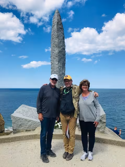 Three tourists posing at Pointe du Hoc monument with ocean views on D-Day Beaches tour