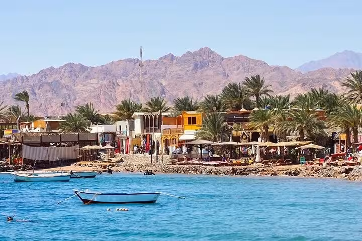 Dahab waterfront with boats, palm trees and mountains, part of Jeep safari canyon Salama and snorkeling tour