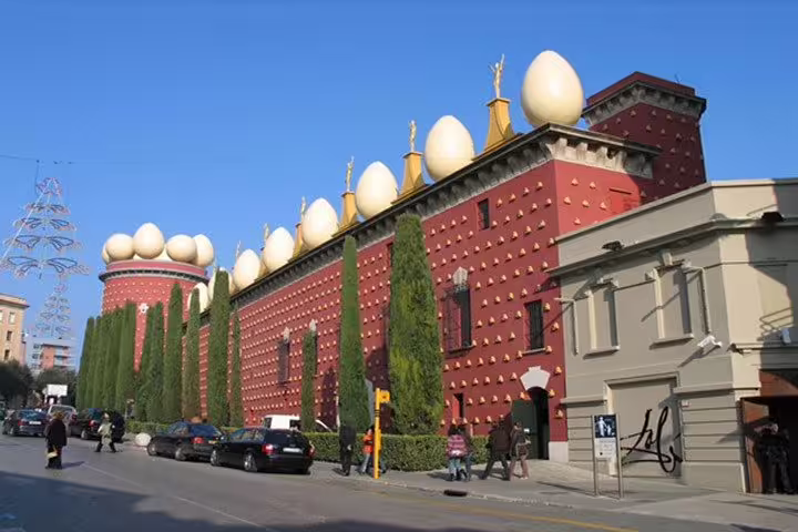 Street view of the Dalí Museum in Figueres, showcasing its unique architecture with egg sculptures and lush greenery.