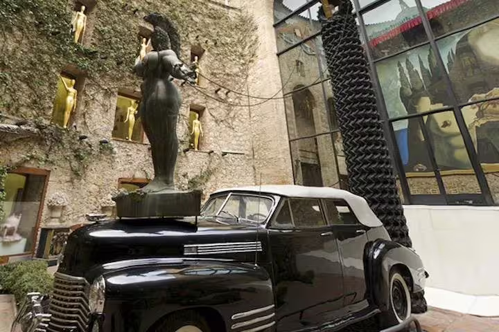 Vintage car with a striking statue at Dalí Museum courtyard, showcasing the creative fusion of art and history.