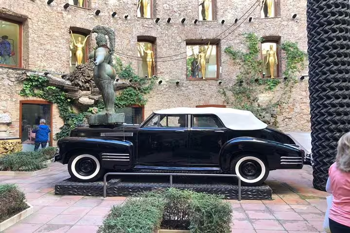 Vintage car display with surrealist sculpture in the courtyard of the Museum Dalí Tour.