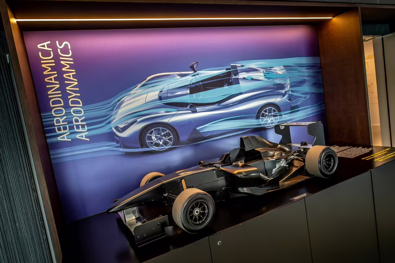 Dallara Academy showcases a sleek race car model against an aerodynamic concept display, highlighting motorsport innovation.