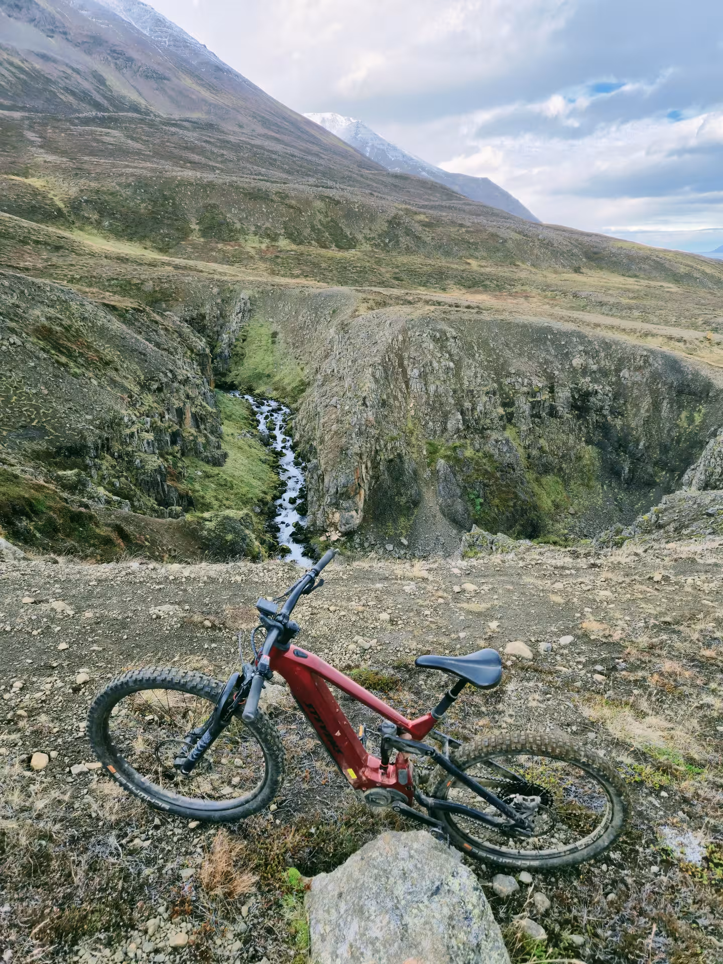 Red e-bike on rocky mountain trail beside a narrow canyon with stream in Dalvik, Iceland