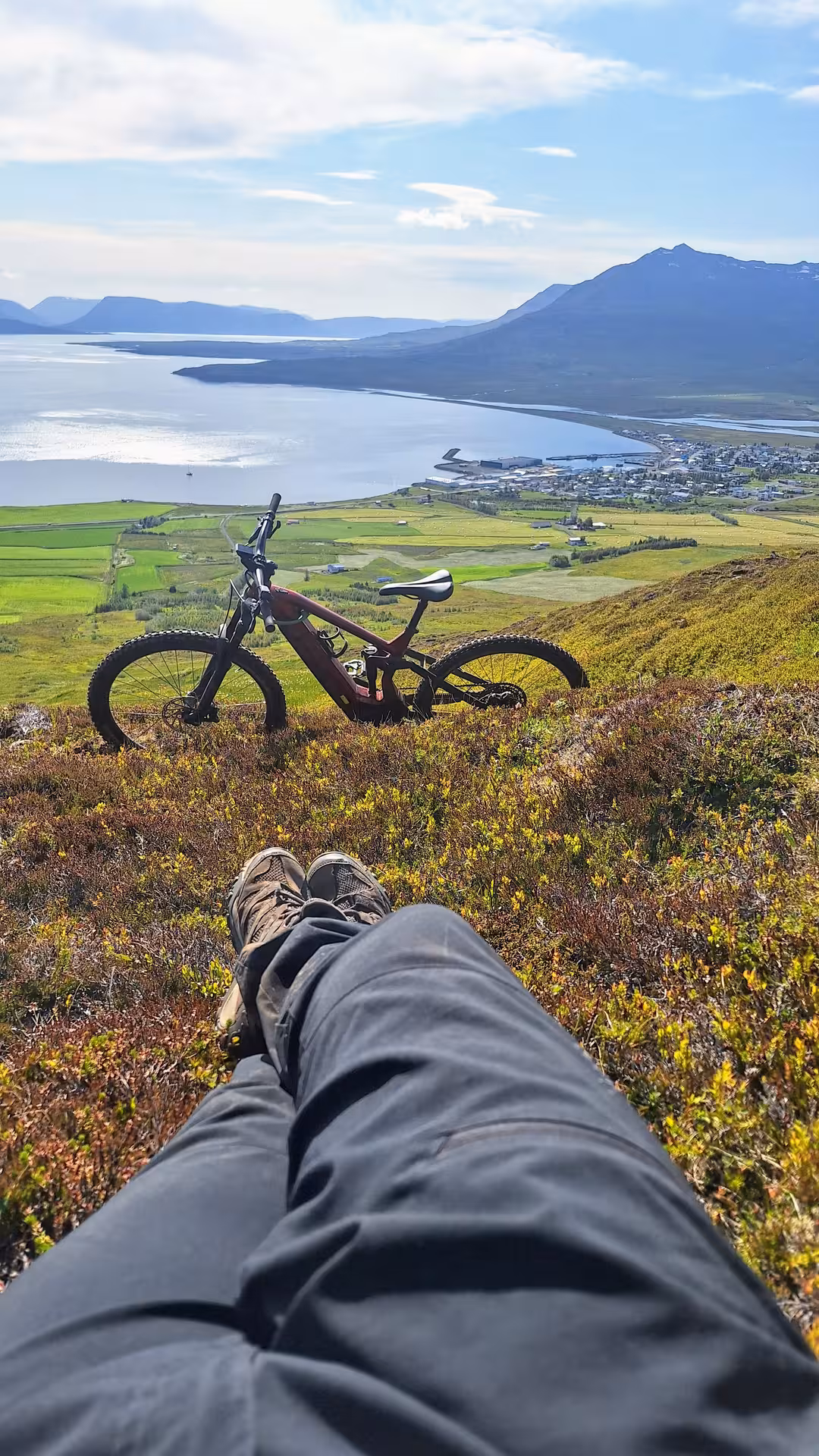 Rider resting on hillside with red e-bike overlooking Dalvik fjord and mountains in Iceland