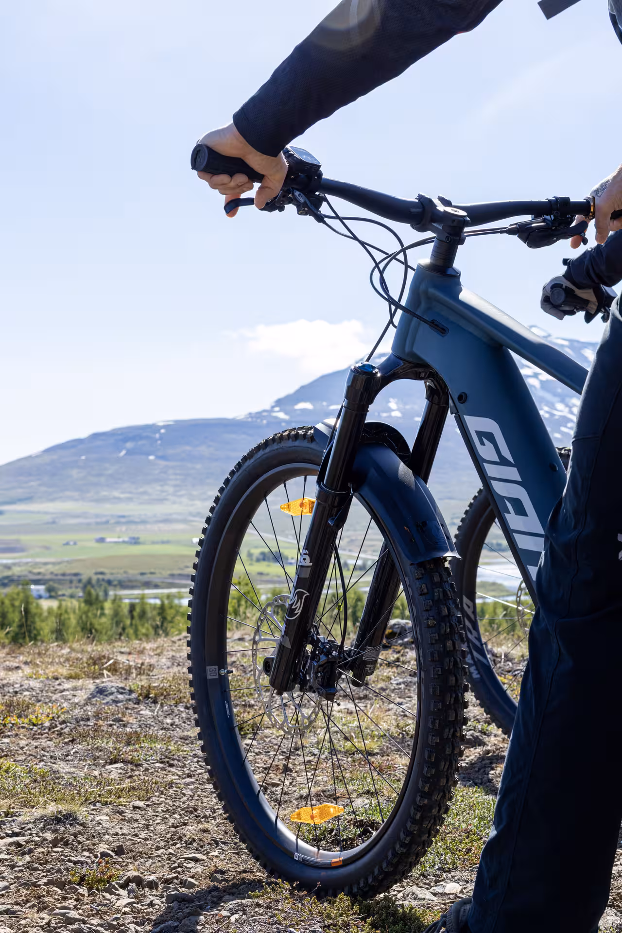 Person holding Giant e-bike handlebars on rocky mountain trail with snow-capped peaks in background