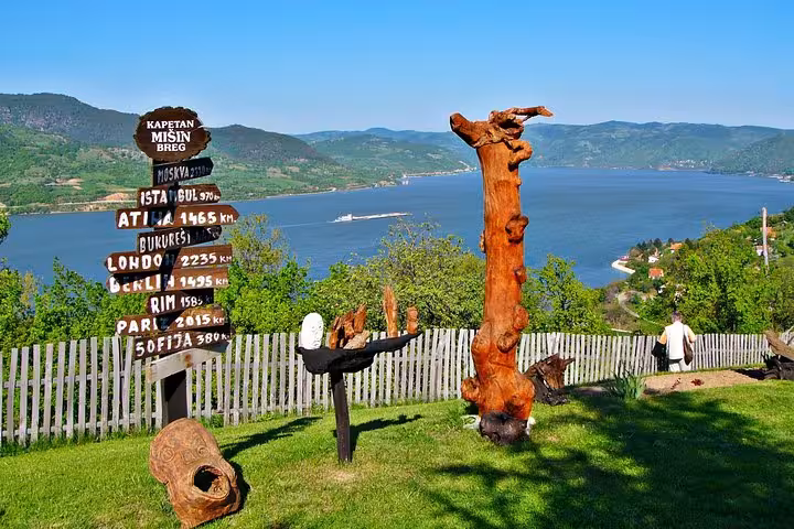 Scenic view from Kapetan Mišin Breg overlooking the Danube River, with wooden sculptures and a distance signpost.