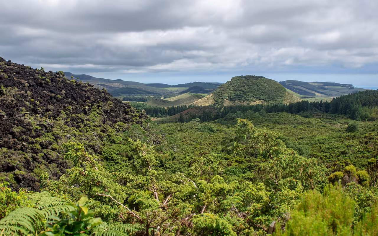 Panoramic view of lush volcanic hills under stormy skies on the Dark Mysteries full-day walking tour