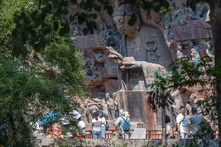 Visitors admire large Buddha sculpture surrounded by detailed carvings at Dazu Rock Carvings in Chongqing, China.