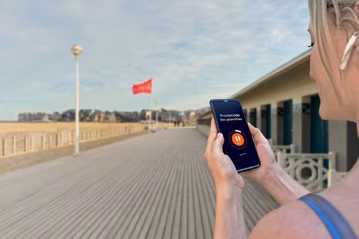 Woman holding smartphone with audio guide app on Deauville's Promenade des Planches boardwalk