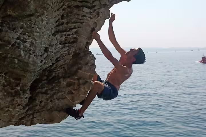 Deep water solo climber on sea cliff above Adriatic near Split, Croatia, guided cliff jumping tour