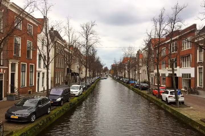 Historic Delft canal lined with red-brick Dutch buildings and bare trees on a cloudy day