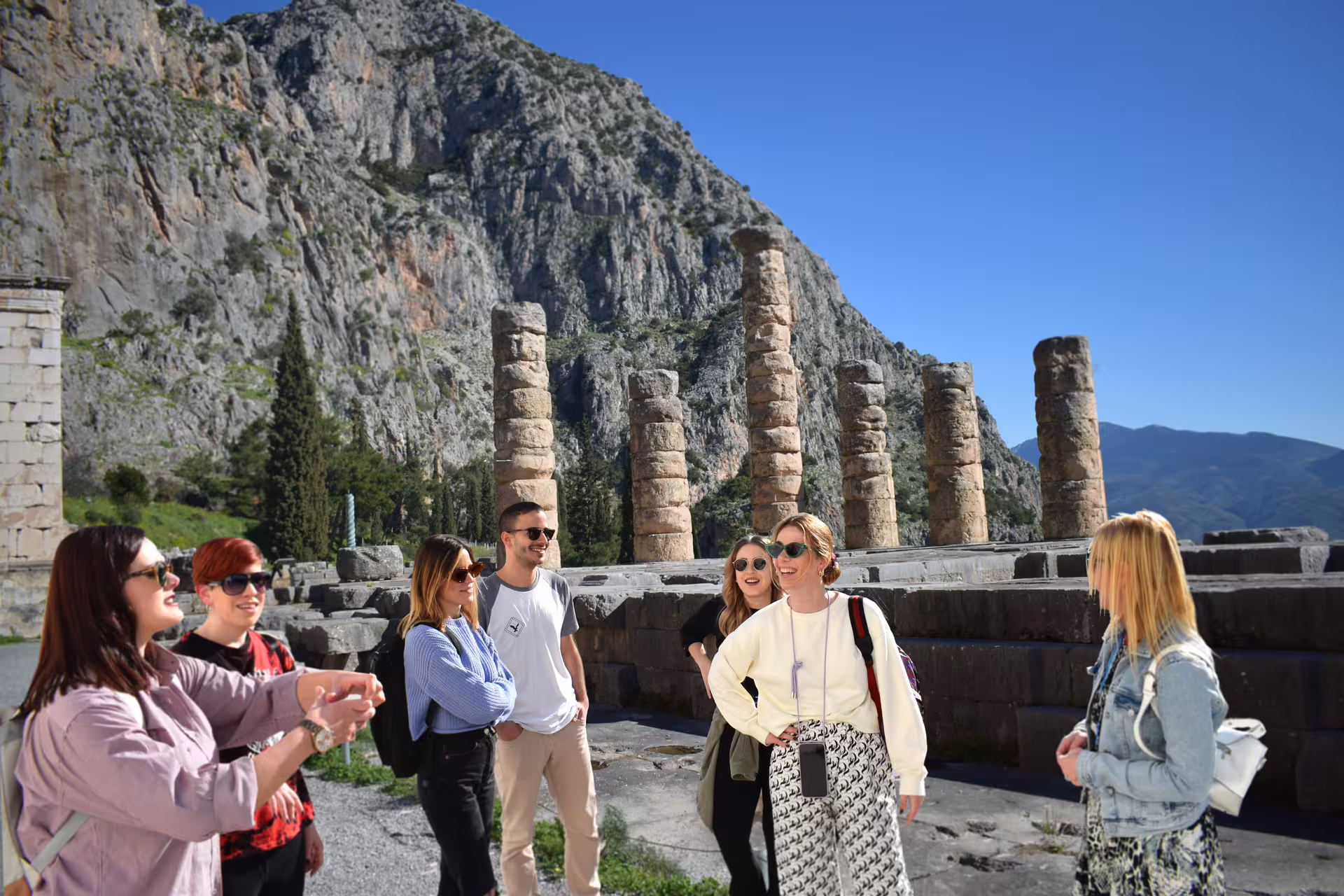 Guided Delphi day trip from Athens with travelers at Temple of Apollo ruins and mountain views in Greece