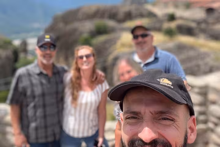 Travelers selfie at Meteora viewpoint with monasteries behind, part of 2-day Delphi and Meteora private trip