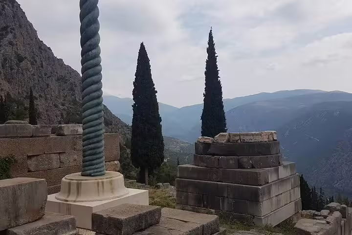 Serpentine column and stone ruins at Delphi with mountain views, stop on a private Delphi day trip from Athens