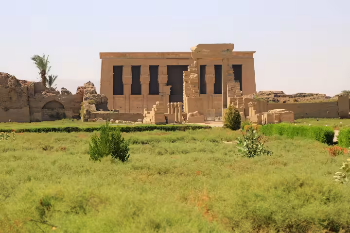 Ancient Dendera Temple facade with columns and hieroglyphs surrounded by green fields in Egypt
