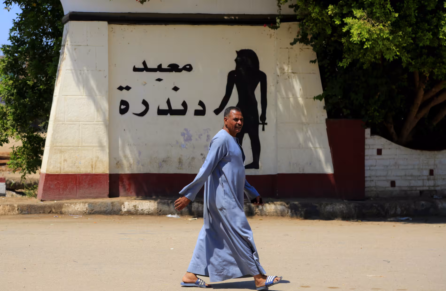 Local man walking past Dendera Temple Arabic sign on a cultural tour from Safaga Egypt