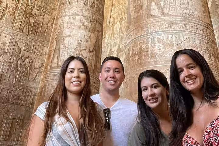 Visitors smiling in front of the ornately carved pillars at Dendera Temple on a private half-day tour from Luxor.