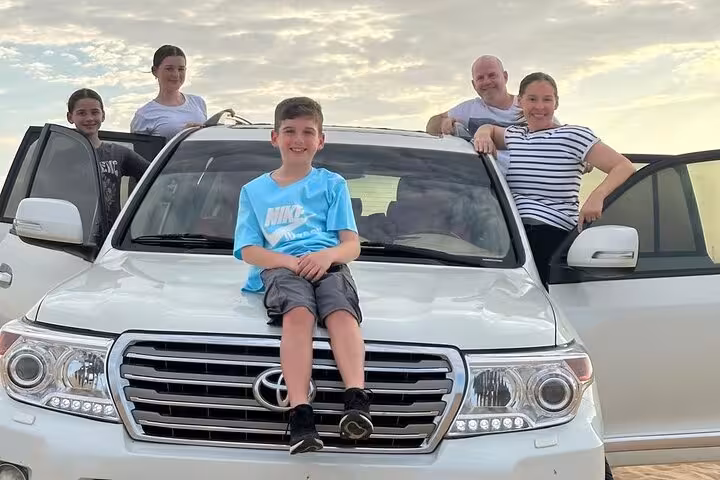 Family posing on 4x4 SUV in Ras Al Khaimah desert safari tour, ready for dune bashing and dinner camp