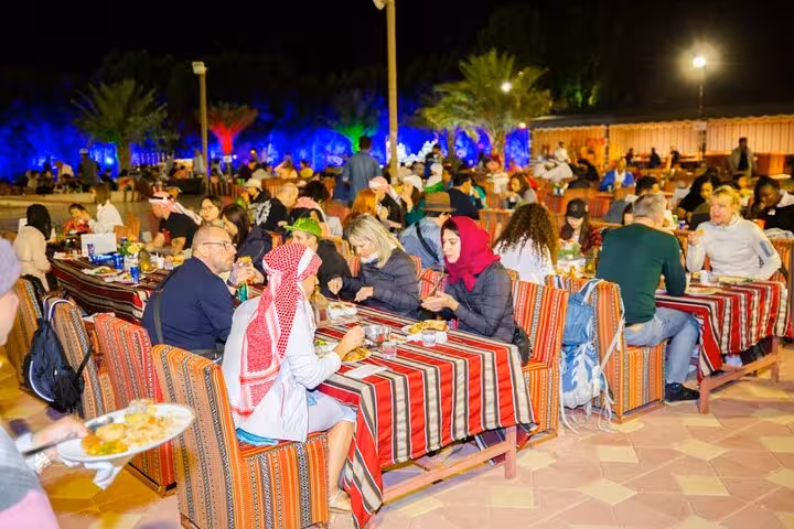 Ras Al Khaimah desert camp buffet dinner with traditional seating, lights and guests after camel ride safari