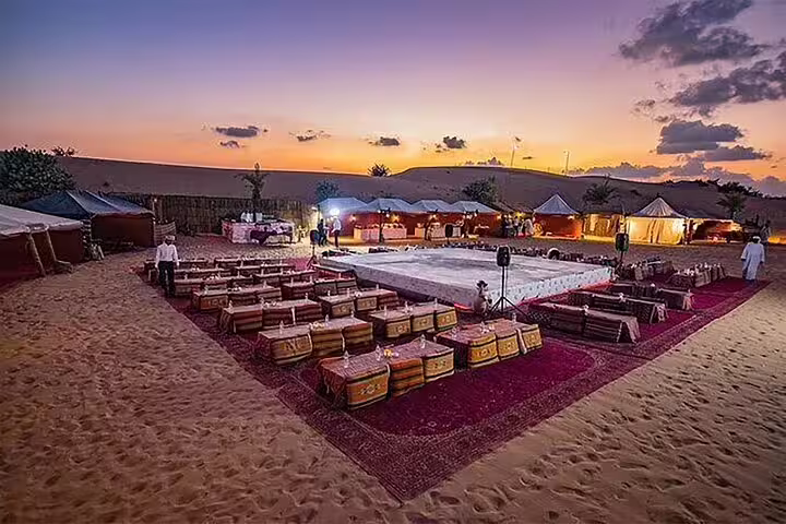 Scenic sunset at a Dubai desert camp set up for a BBQ dinner with traditional seating, awaiting live entertainment and shows.